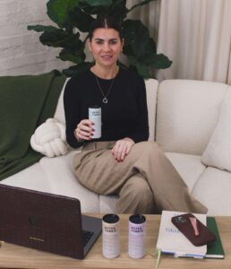 E2 founder, Queenie Porter, sitting on a cream sofa smiling with a can of Water Junkie